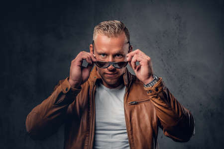 Handsome blond, muscular male in sunglasses, dressed in a white t shirt and brown leather jacket.の写真素材