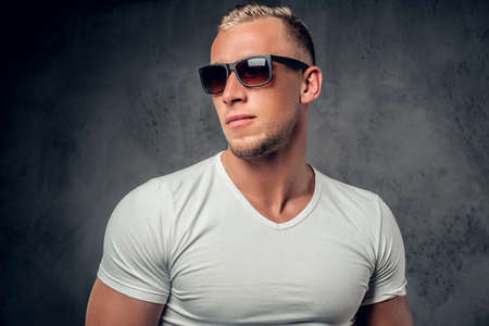 Handsome blond male in sunglasses and white t shirt posing over grey background in a studio.の写真素材