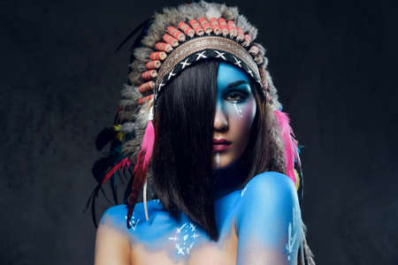 Close up portrait of shamanic female with Indian feather hat and colorful makeup.の写真素材