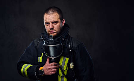 Studio portrait of a male dressed in a firefighter uniform holds an oxygen mask.