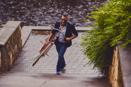 Redhead bearded male dressed in a blue jacket and jeans on a retro bicycle in a park.