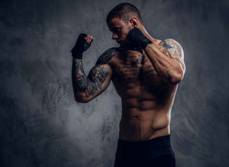 Studio portrait of shirtless, tattooed fighter male over grey vignette background.の写真素材
