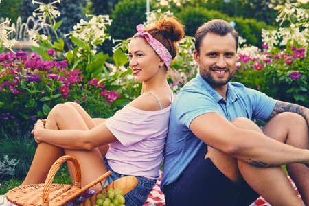 Attractive tattooed, bearded male and a redhead female lying on a blanket on a lawn in a park. Picnic time.の写真素材