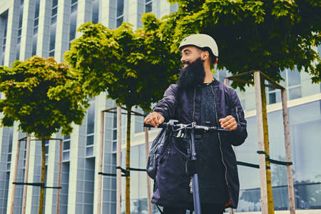 Stylish bearded male in sunglasses posing on electric scooter in over modern building background.の写真素材