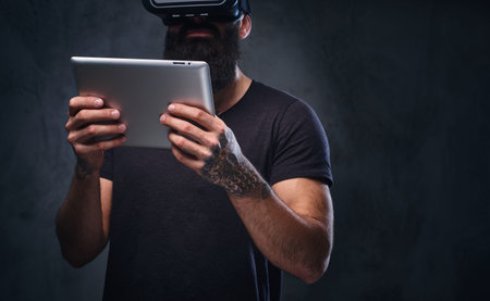 A man with tattoos on his arms wearing VR glasses and holds tablet PC.の写真素材