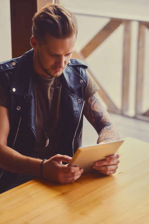 Attractive guy dressed in leather jacket using a tablet PC in a cafe near the window.の写真素材
