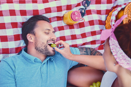 Attractive tattooed, bearded male and a redhead female lying on a blanket on a lawn in a park....