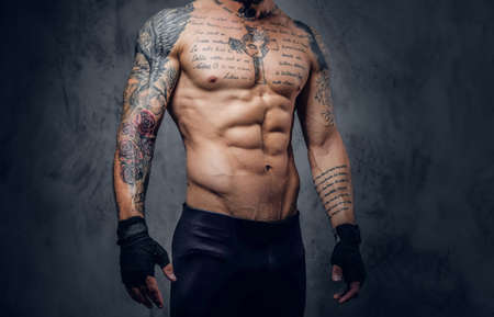 Studio portrait of muscular, shirtless, tattooed male over grey background.の写真素材
