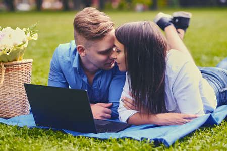 Attractive couple lying on a blanket on a lawn and is using a laptop on a picnic.の写真素材