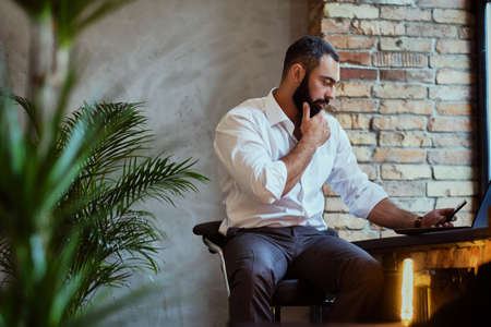 Bearded modern male using smartphone in a room with loft interior.の写真素材