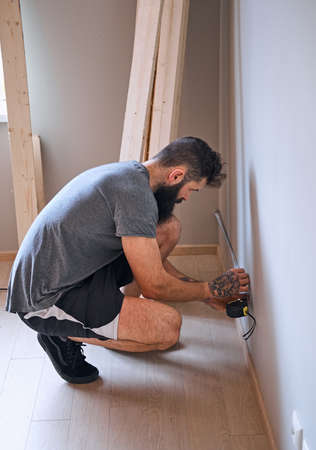 Bearded carpenter with tattoo on his arm measuring a wall.の写真素材