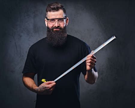 Bearded worker holds the measure line over grey background.