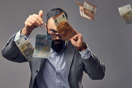 Bearded male dressed in a suit catch money banknote in the air.