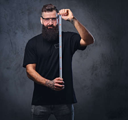 Bearded worker holds the measure line over grey background.の写真素材