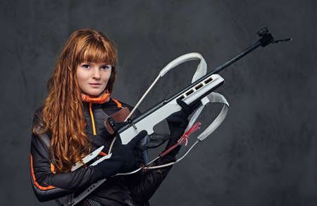 Studio portrait of a redhead female Biathlon champion holds a gun over grey background.の写真素材