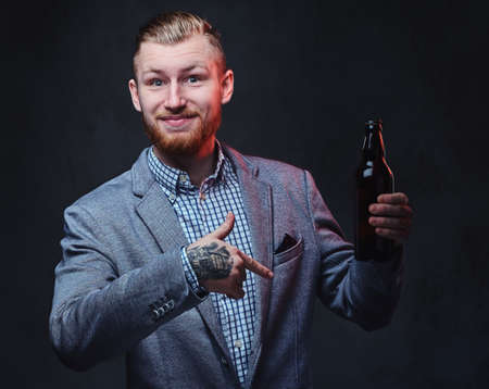 A man dressed in a suit holds a bottle with craft beer.