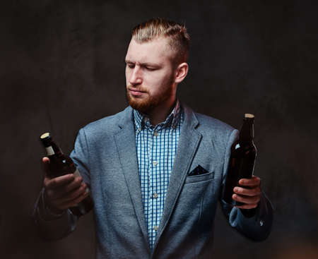 A man dressed in a suit holds a bottle with craft beer.