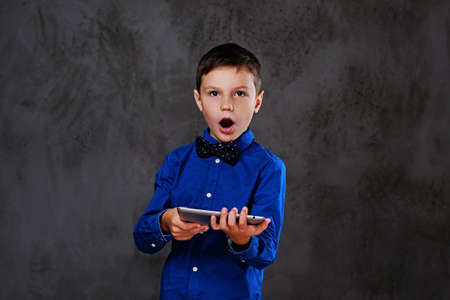 The positive teenager boy holds tablet PC over grey background.の写真素材