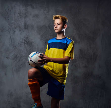 Portrait of blond teenager, soccer player dressed in a yellow uniform plays with a ball.の写真素材
