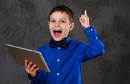 The positive teenager boy holds tablet PC over grey background.の写真素材