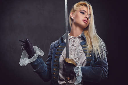 An attractive blonde female dressed in medieval urban clothes holds a silver sword over grey background.の写真素材