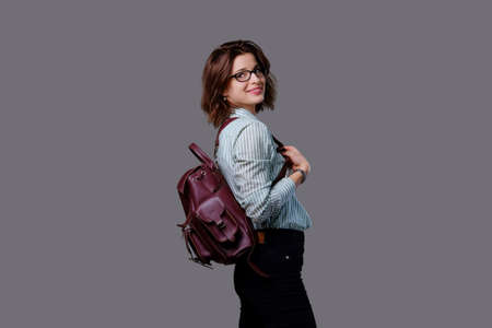 Positive young traveler female with leather backpack isolated on grey background.の写真素材