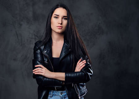 A fashionable brunette female dressed in a black leather jacket and a jeans over dark grey background.の写真素材