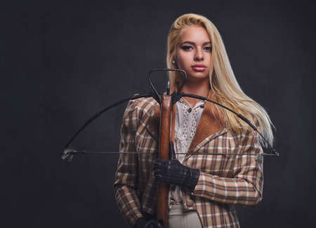Studio portrait of blond old fashioned female holds a crossbow over grey background.の写真素材