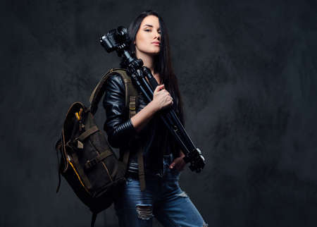 Brunette female photographer holds professional camera on a tripod and traveler backpack.の写真素材