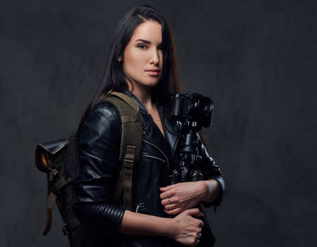 Brunette female photographer holds professional camera on a tripod and traveler backpack.の写真素材