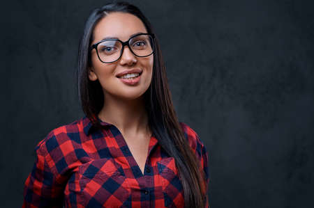 Studio portrait of brunette female in eyeglasses dressed in a red shirt over grey background.