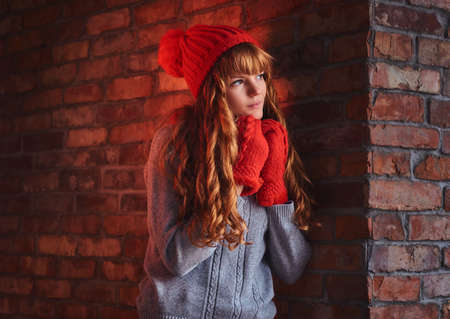 An attractive redhead female  posing over the wall of a red bric