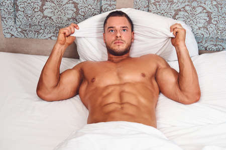 A handsome nude man lying in a bed.