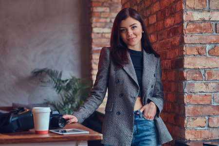 Portrait of a young female photographer standing against a brick