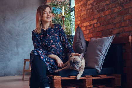 Happy woman sitting with a cute pug in a room with loft interiorの写真素材