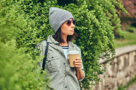 Portrait of a brunette hipster relaxing in a city park with coffの写真素材