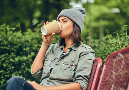 A hipster woman in hat sitting on a bench in a city park. Relaxing in nature.の写真素材