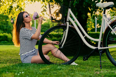 Beautiful brunette sits on the green lawn with bicycleの写真素材