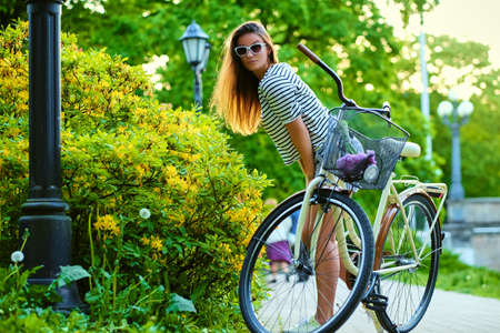 An attractive brunette female with a bicycle sniffing flowersの写真素材