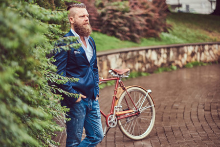 Male dressed in casual clothes, standing with a retro bicycle in a park.の写真素材