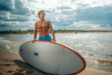 Surfer male with a muscular body with his surfboard at the beach.の写真素材