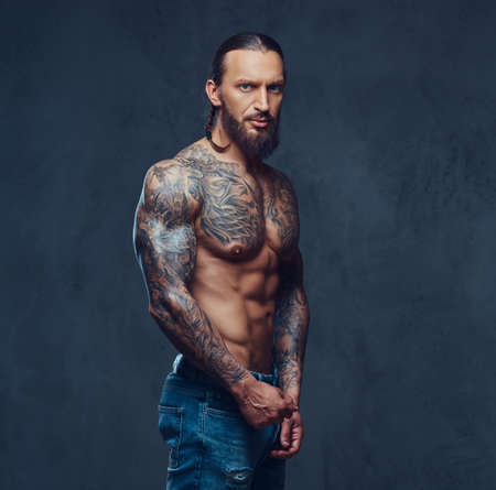 Close-up portrait of a muscular naked bearded tattoed male with a stylish haircut, isolated on a dark background.の写真素材