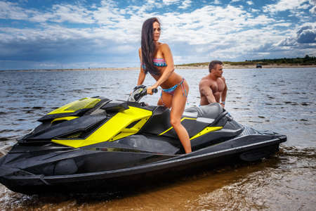Attractive couple of a sexy girl and shirtless muscular male have fun with a jet ski on a seacoast.の写真素材
