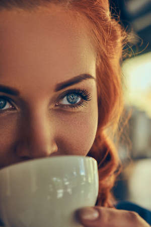 A beauty redhead female barista drinks a coffee, at the coffee shop.の写真素材