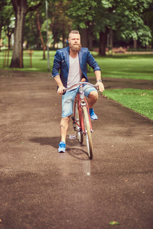 Portrait of a bearded male with a haircut dressed in casual clothes riding a bicycle in a park.の写真素材