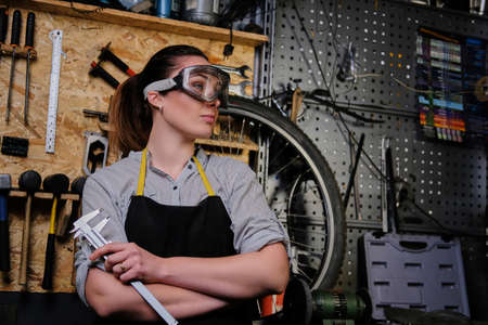 Portrait of a beautiful brunette female wearing working clothes, apron and goggles, standing in a workshop.の写真素材