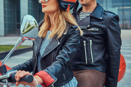 An attractive couple, a handsome man and sexy female riding together on a red retro scooter in a city.の写真素材