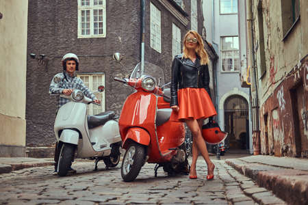 Attractive couple, a handsome man and sexy female standing on an old street with two retro scooters.の写真素材