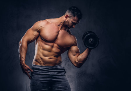 Tall stylish shirtless bodybuilder dressed in sports shorts, doing exercise on a bicep with a...
