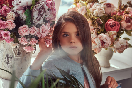 Portrait of a cute little girl with long brown hair and piercing glance wearing a stylish dress,...